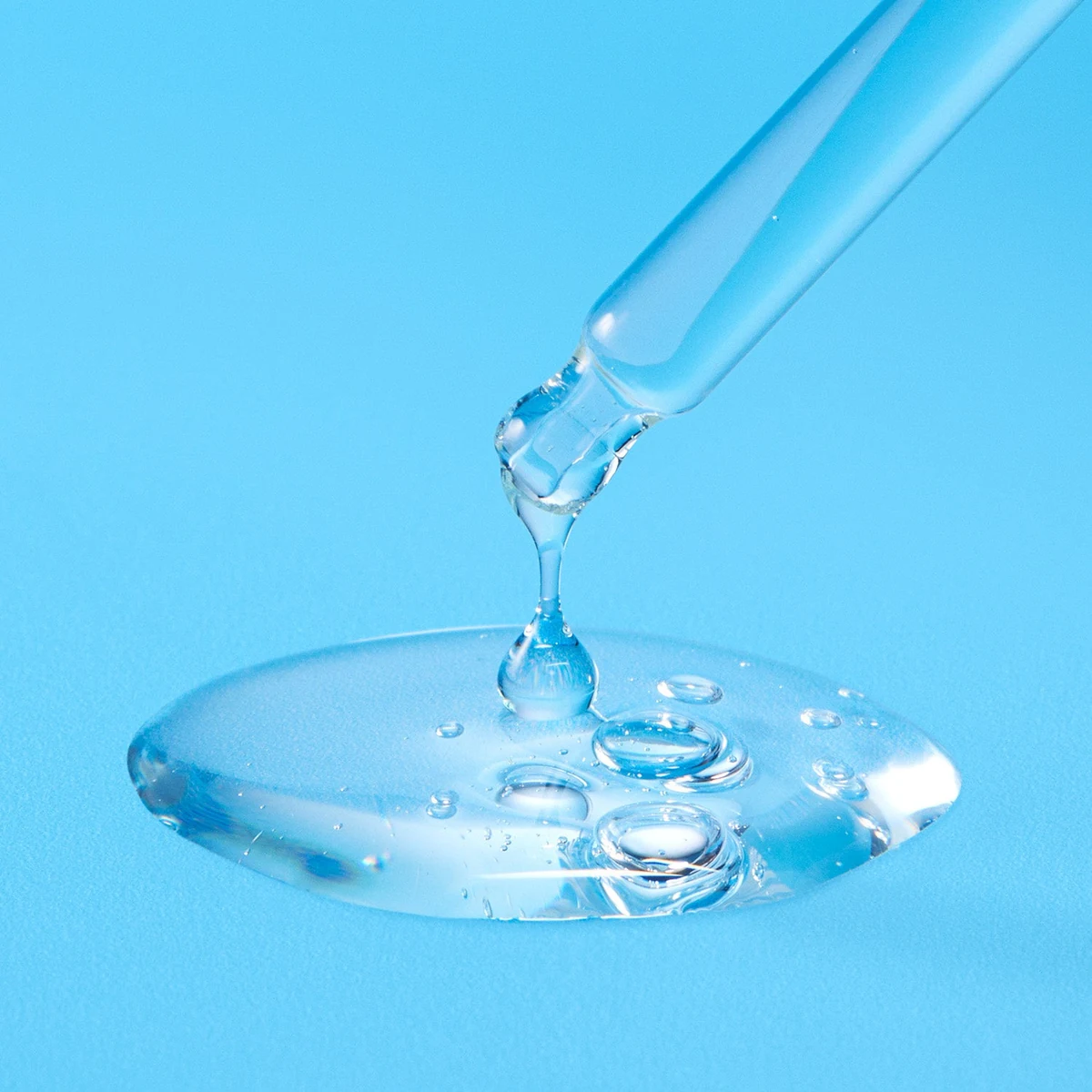 Torriden DIVE IN Serum dropper releasing clear, watery serum onto a light blue surface
